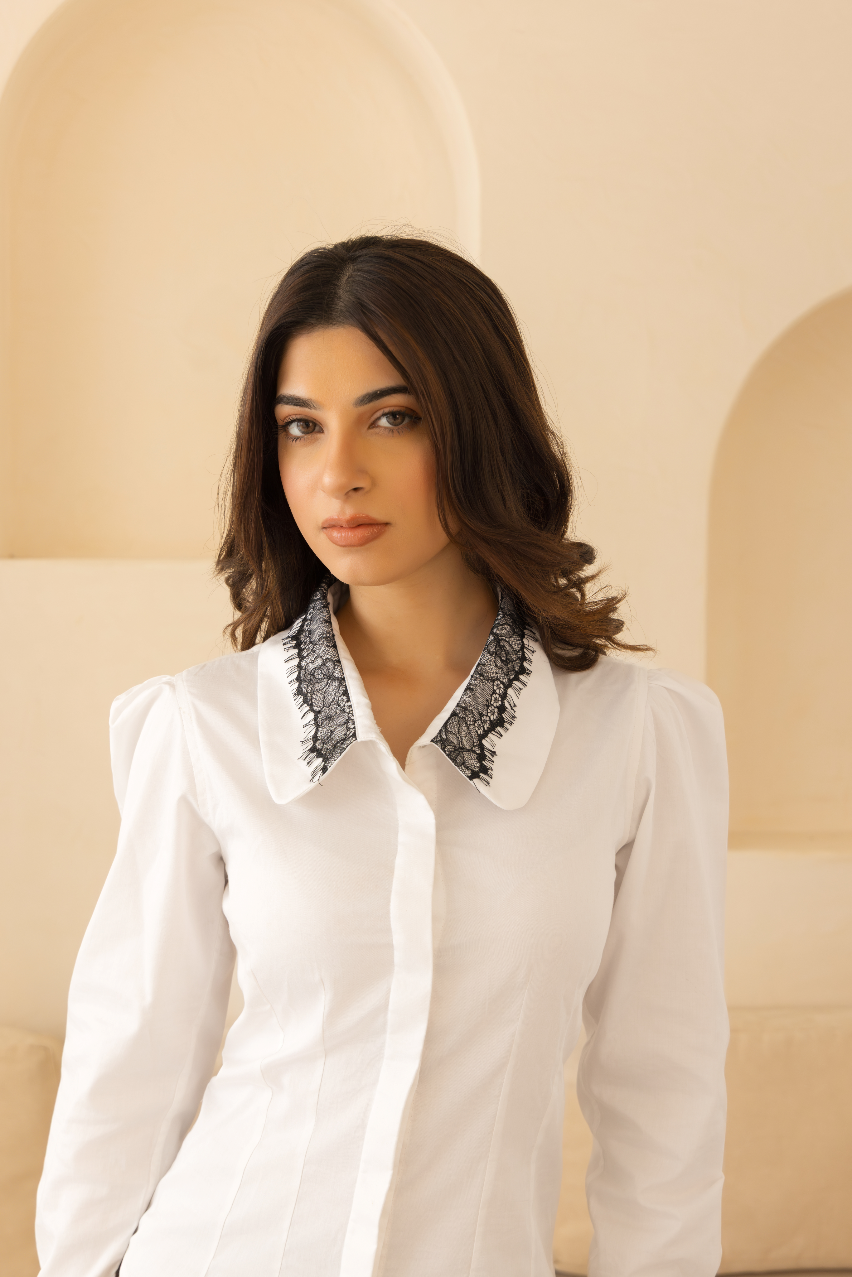 Woman wearing a white blouse with black lace collar in a softly lit room.