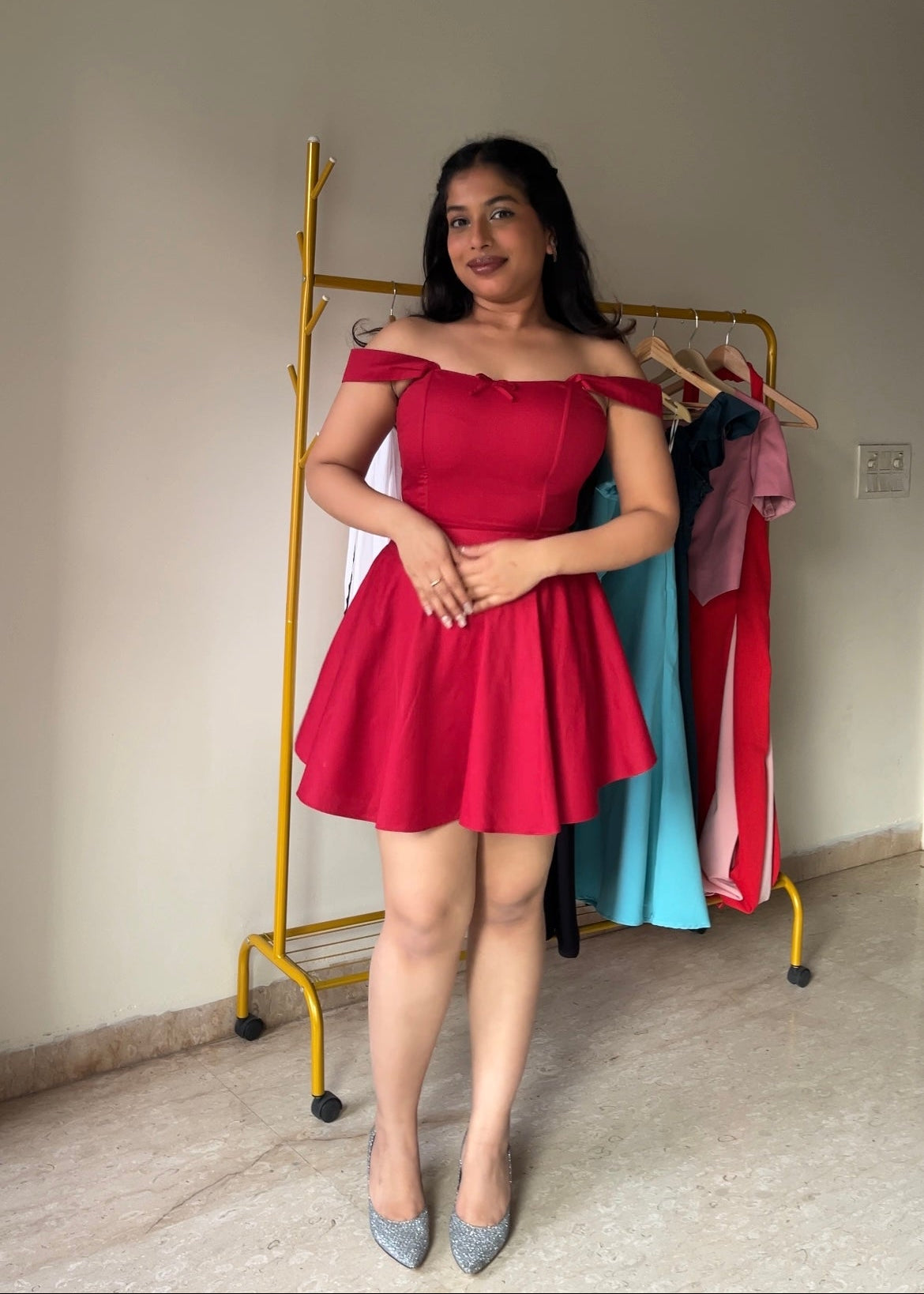 Woman in a red dress standing in front of a clothing rack with other dresses.