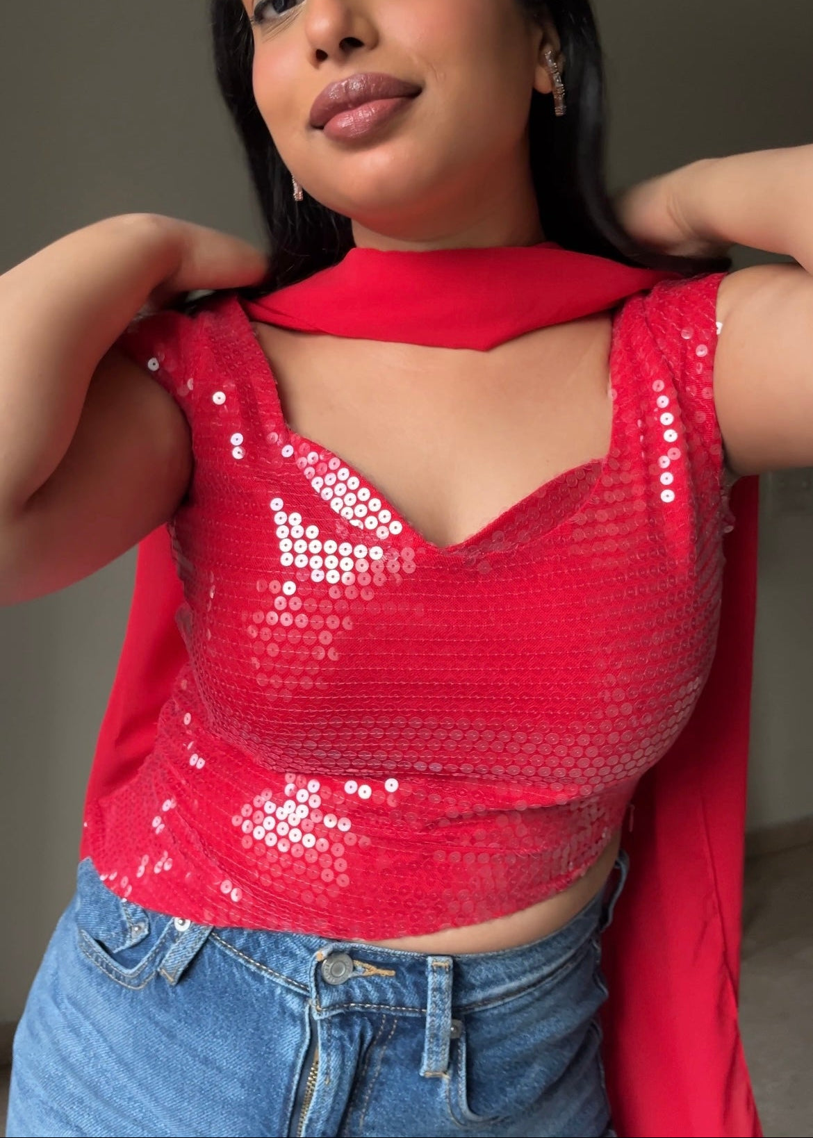 Woman wearing a red sequin top and blue jeans indoors.