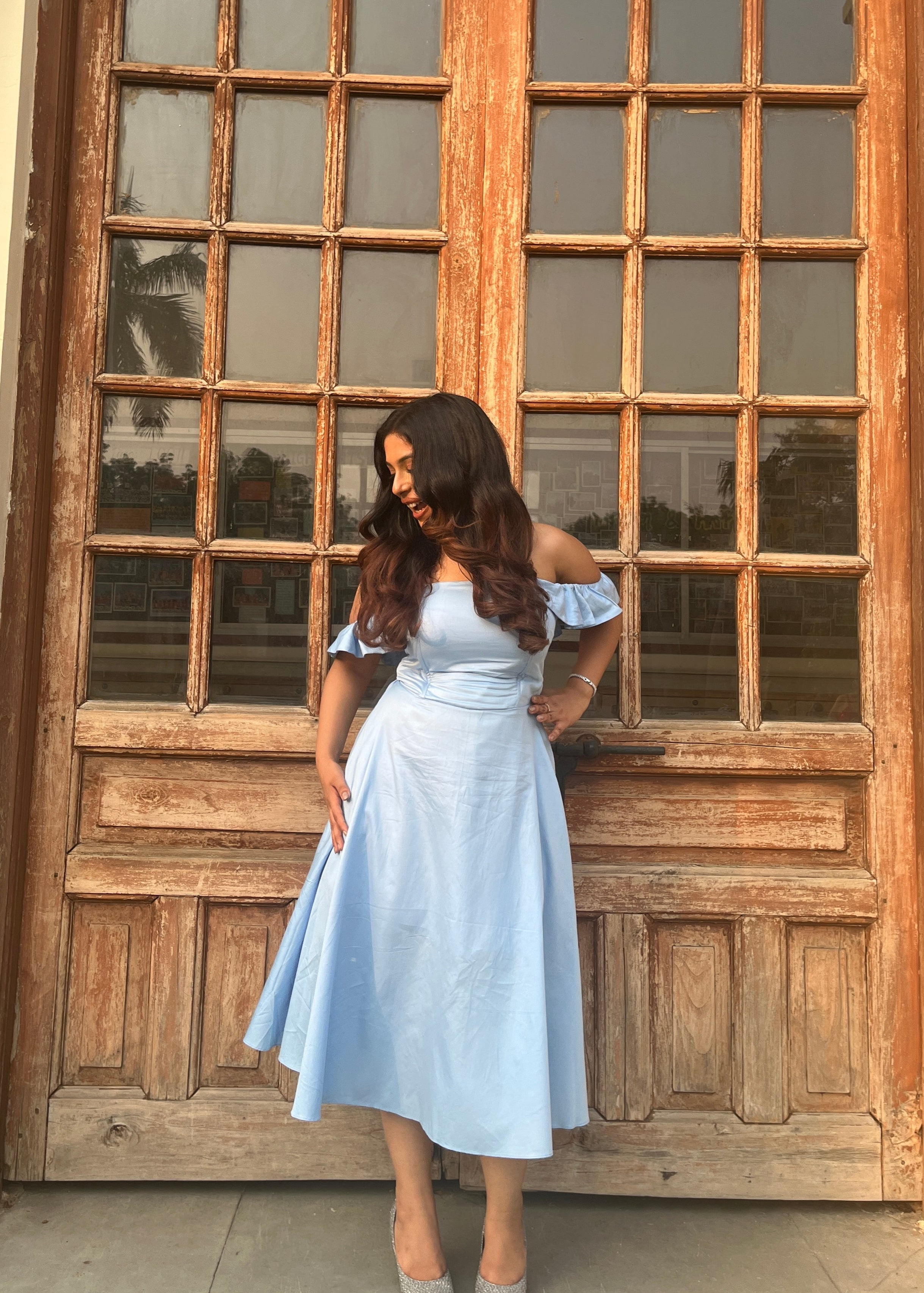 Woman in a light blue dress standing in front of a large wooden door with glass panels.