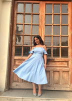 Woman in a light blue dress standing in front of a wooden door with glass panels.