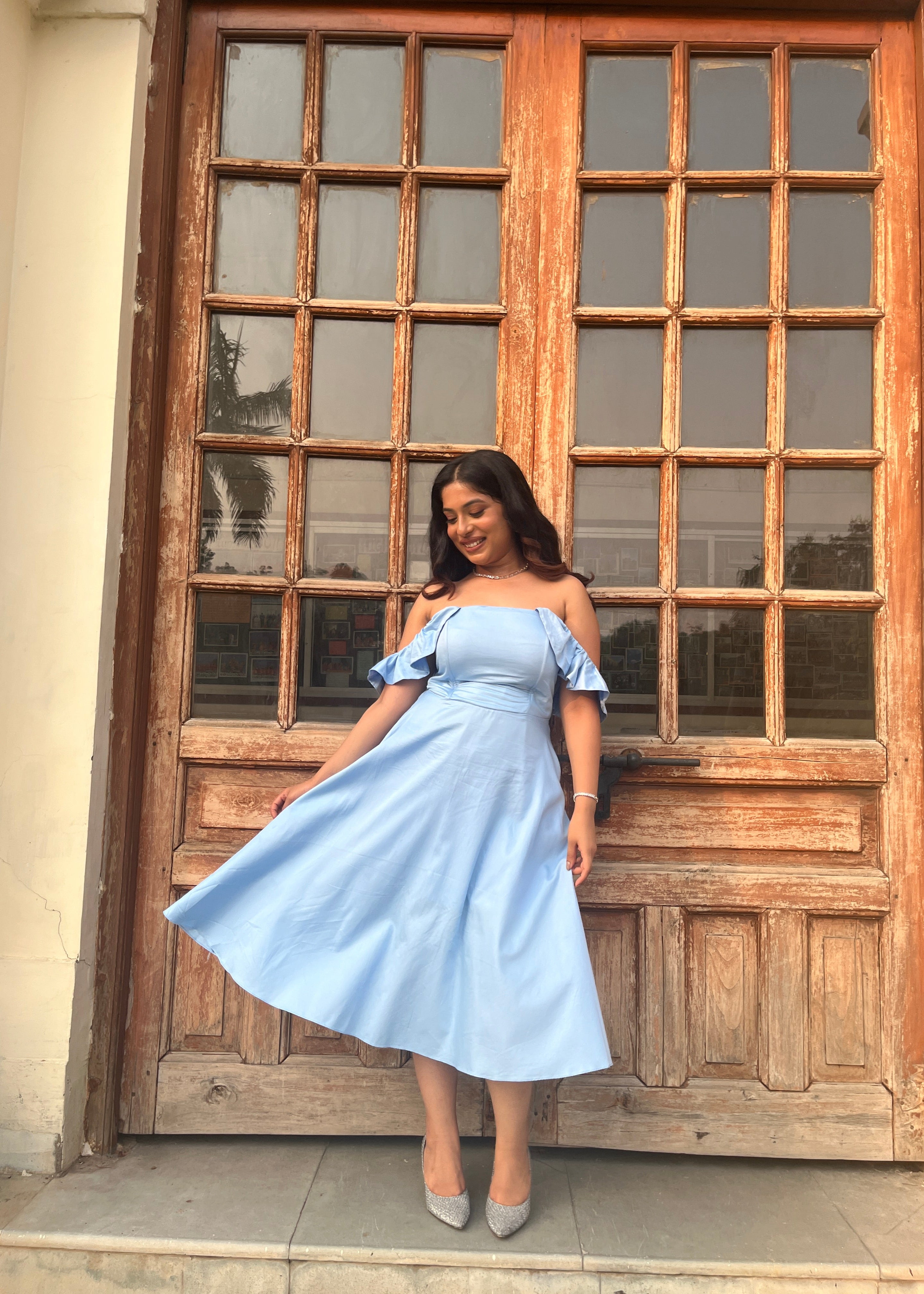 Woman in a light blue dress standing in front of a wooden door with glass panels.