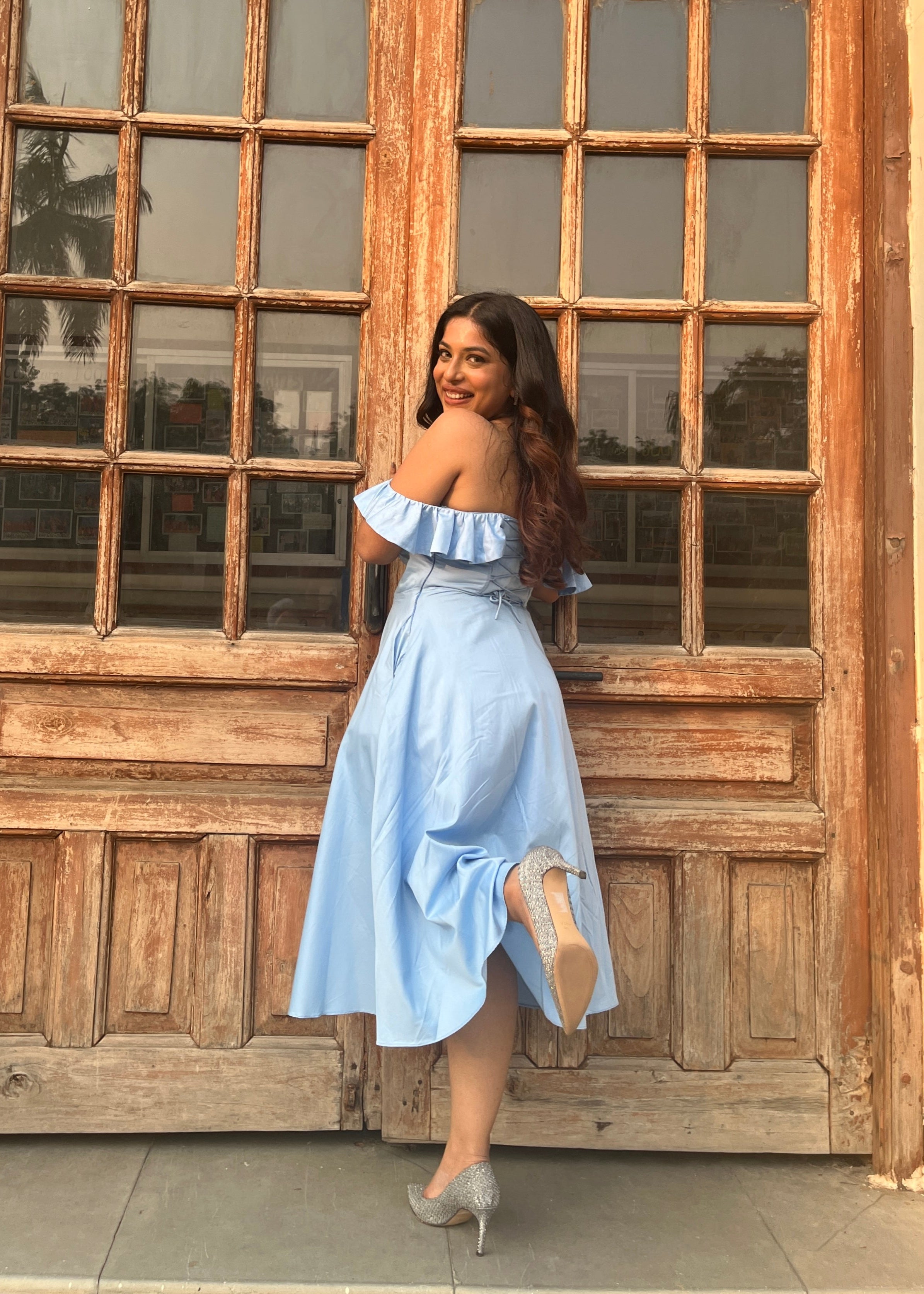 Woman in a light blue dress standing in front of a wooden door