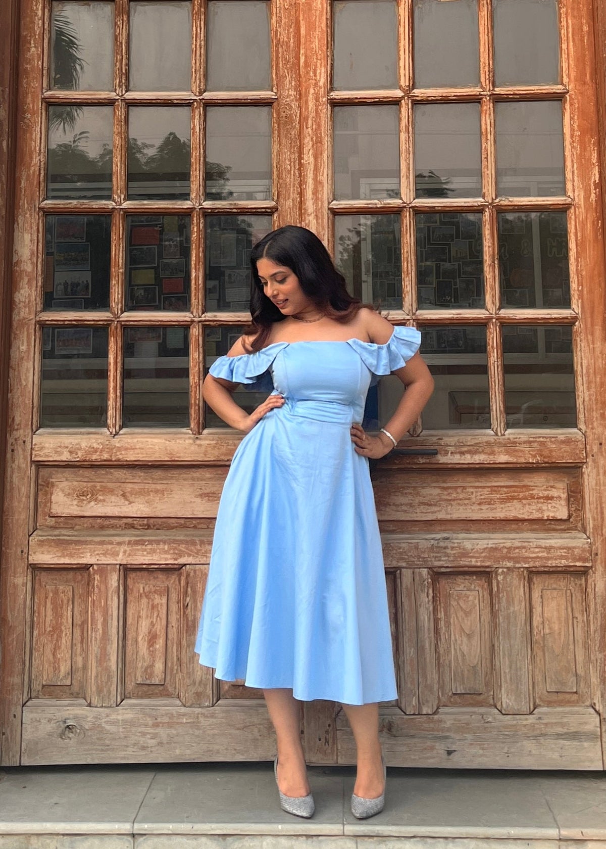 Woman in a light blue dress standing in front of a wooden door.