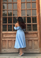 Woman in a light blue dress standing in front of a large wooden door with glass panels.
