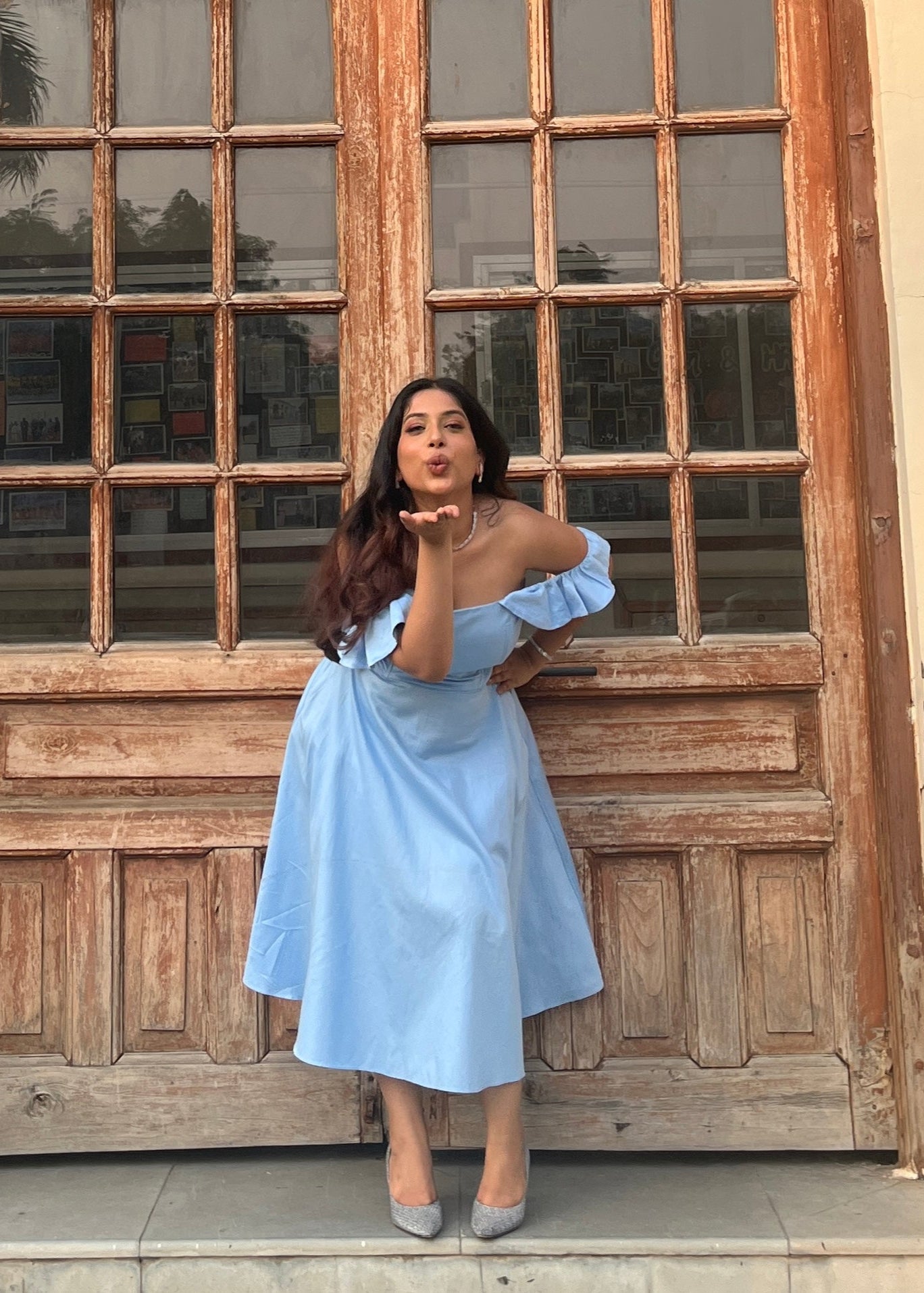 Woman in a light blue dress standing in front of a wooden door