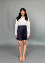 A woman wearing a white Dorothea lace shirt with lantern sleeves and a neck-tie, paired with a dark skirt and beige shoes.