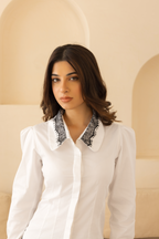 Woman wearing a white blouse with black lace collar in a softly lit room.