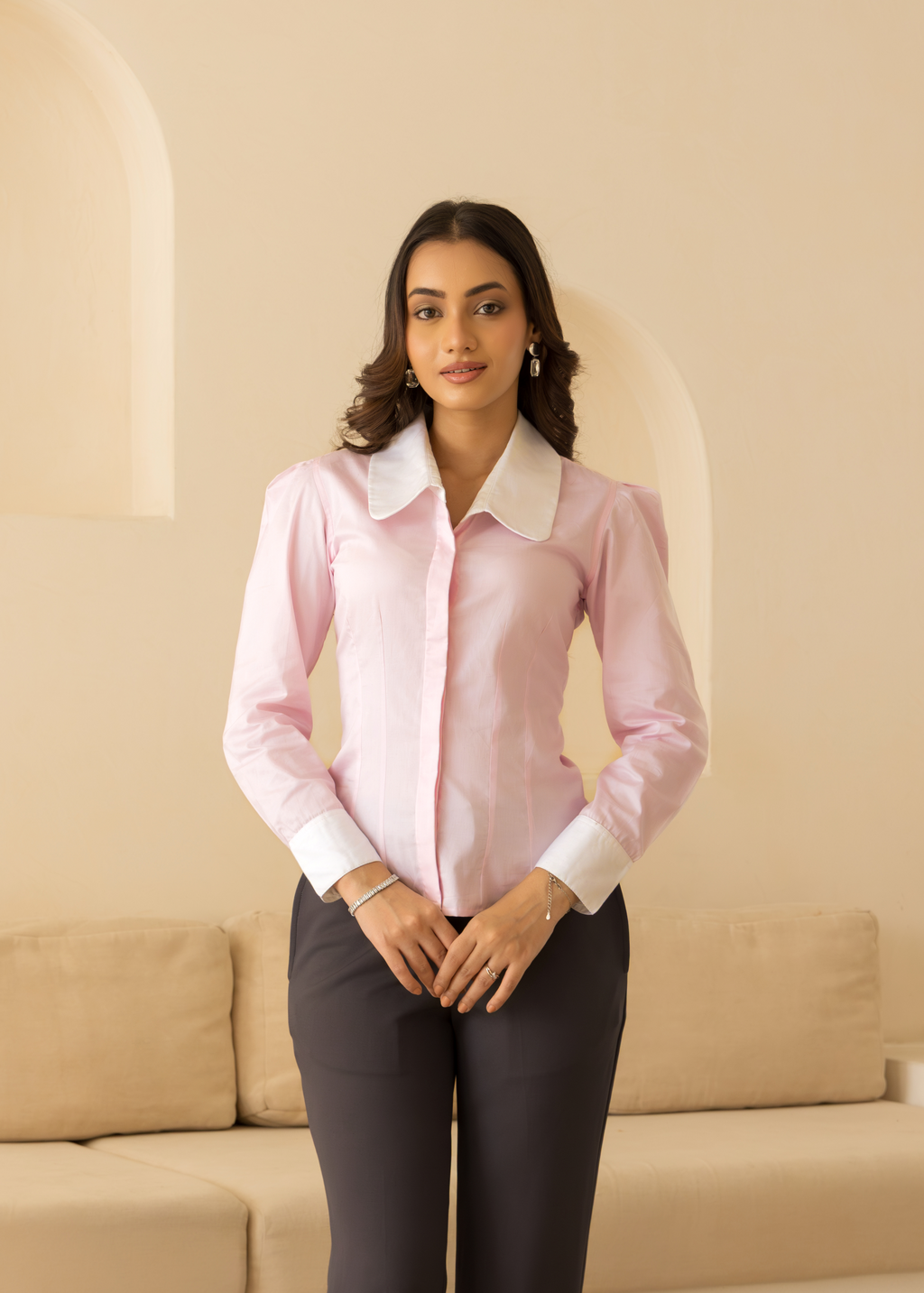 Woman wearing a pink blouse and dark pants in a room with beige walls and furniture.