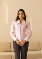 Woman wearing a pink blouse and dark pants in a room with beige walls and furniture.