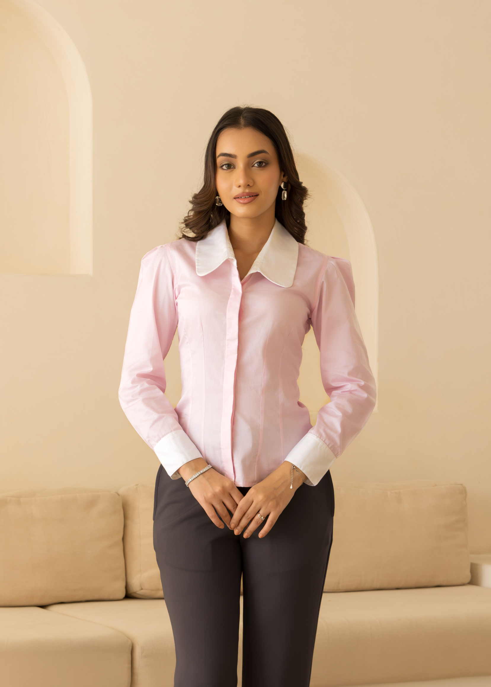 Woman wearing a pink blouse and dark pants in a room with beige walls and furniture.