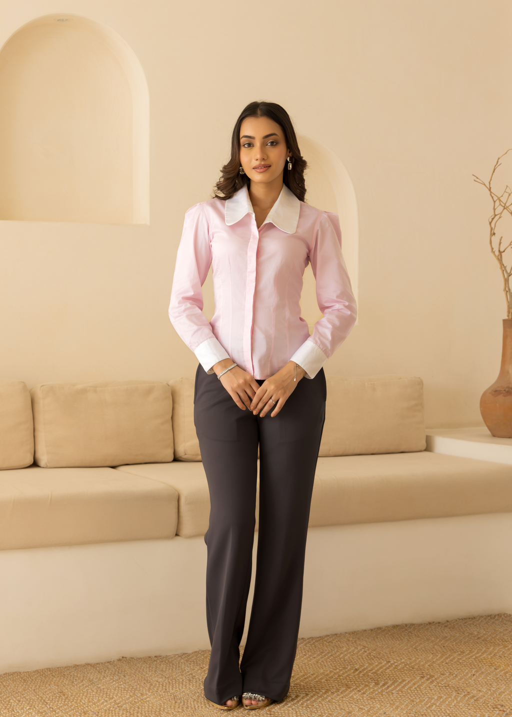 Woman wearing a pink blouse and dark pants in a room with beige walls and furniture.